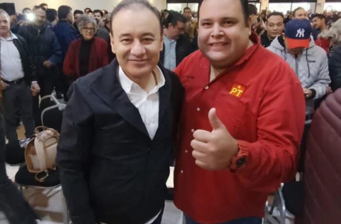Dos asistentes posan durante un encuentro político en Hermosillo; uno viste una camisa roja con el emblema del PT