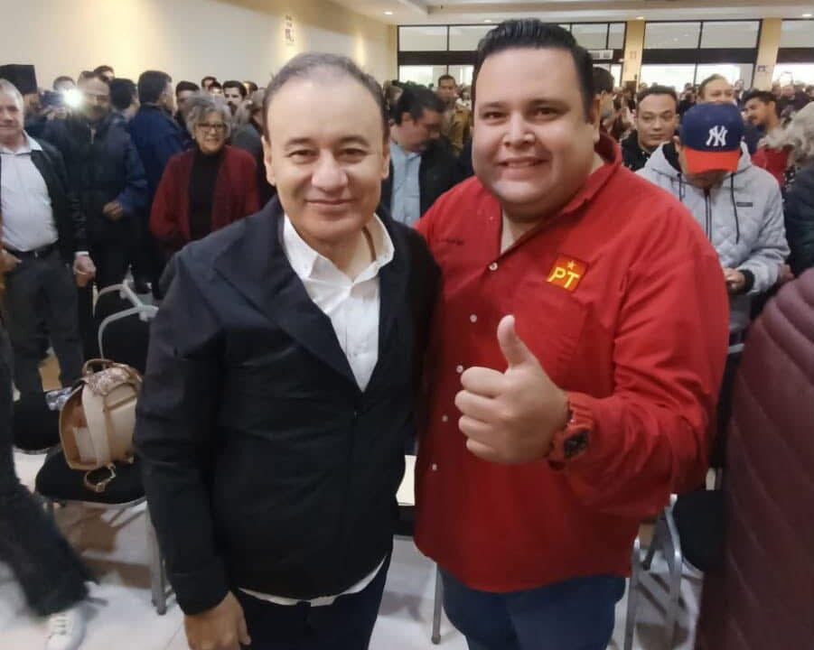 Dos asistentes posan durante un encuentro político en Hermosillo; uno viste una camisa roja con el emblema del PT